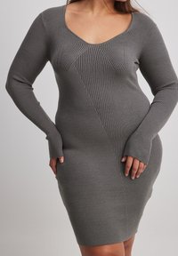 Abito bodycon a coste in grigio con scollatura a V profonda, maniche lunghe e dettagli di cucitura diagonale. Realizzato in tessuto a maglia elasticizzato.
