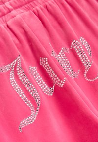 Roza žametna tkanina s kristalnimi okrasnimi detajli razporejenimi v dekorativnem vzorcu. Tekstura izgleda mehko in udobno.