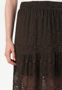 Brun lagdelt skjørt med teksturert stoff og bølgete broderte mønstre, samt elastisk midje, som gir en lett og luftig design.