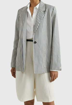Kvinde iført en hvid bluse, hvide shorts og en enkeltknappet blazer med lodrette marineblå og hvide striber.