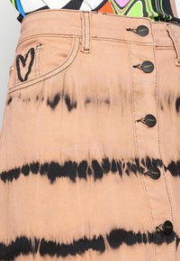 Saia de ganga em rosa claro com riscas de tie-dye pretas, apresentando um fecho frontal com botões e um detalhe em forma de coração no bolso.