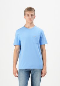 Világoskék pamut póló kerek nyakkal, rövid ujjú, bal mellel zsebbel. Simább textúra és laza szabás.