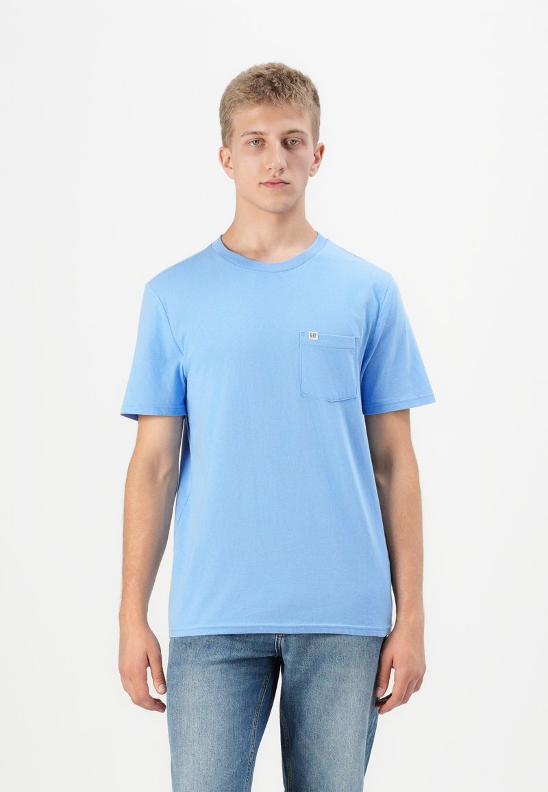 Világoskék pamut póló kerek nyakkal, rövid ujjú, bal mellel zsebbel. Simább textúra és laza szabás.