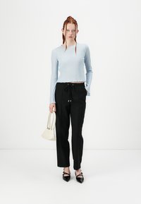 Lys blå ribbet langærmet top kombineret med sorte bukser med snoretræk. Modellen holder en lille hvid handbag og har sorte spidse sko på.