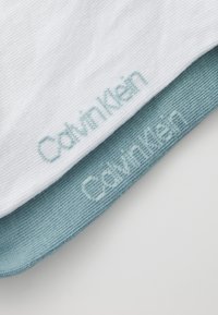 Calcetines de mezcla de algodón blancos con una sección del pie en azul claro, con el logotipo bordado de "Calvin Klein" en un color a juego en ambos.