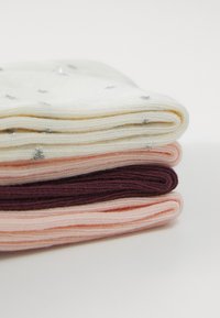 Vier übereinander gestapelte Paar bequeme Socken in Creme, Hellrosa, zartem Pfirsich und tiefem Burgunder, mit metallischen silbernen Akzenten auf dem Cremer Paar.