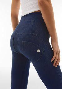 Leggings blu navy con una superficie lucida e texturizzata. Presentano un alto punto vita e due tasche posteriori, una delle quali ha un'etichetta con logo.