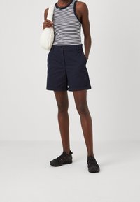 Granatowe szorty z podwiniętymi brzegami, zestawione z czarno-białą tank topem w paski. Dodatkiem jest mała biała torebka. Obuwie to czarne sandały.