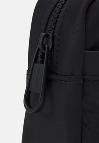Zaino nero realizzato in nylon testurizzato, con una zip dettagliata e un'etichetta del logo intagliata. Il design sottolinea funzionalità e durabilità.