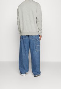 Grå sweatshirt med rund hals, långa ärmar och ribbad nederkant; ihop med löst sittande, blekblå denim cargo-byxor med stora fickor.