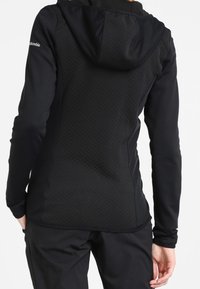 Giacca in pile nera con retro texture, design aderente e cappuccio. Presenta una parte anteriore liscia e il logo Columbia sulla spalla.