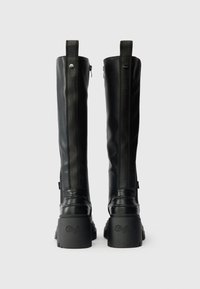 Černé kozačky do půli lýtek s hladkým koženým povrchem, zvýšenými platformami a postranními zipy. Obsahují detaily loga na podpatku a na holeni.