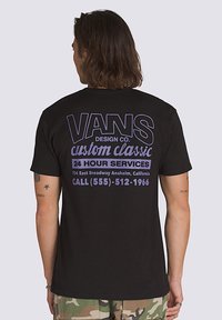 Camiseta de algodón negra con gran texto blanco y morado en la parte posterior, con un logo y detalles de contacto. Diseño de mangas cortas y cuello redondo.