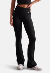 Black ribbed flared leggings with a high waistband, featuring a small logo detail at the front and a smooth, stretchy fabric texture.
