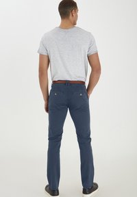 Námornícky modré chinos nohavice so slimm fit, štruktúrovaná tkanina, dizajn s piatimi vreckami a hnedý opasok, v kombinácii s svetlo šedou košeľou s krátkym rukávom.