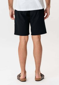 Sorte bomuldsbukser, knælange, med en afslappet pasform. Sættet med brune sandaler med blød tekstur og dekorative detaljer.