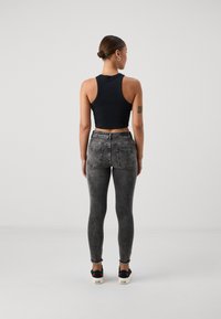Sort cropped tank top, grå skinny jeans med falmede mønster og sorte sko med grønne og røde accenter. Glat stof og tætsiddende design.