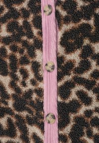 Gros plan d'une veste imprimé léopard texturée avec des taches beiges et noires, dotée d'une patte de boutonnage côtelée rose et de trois boutons ronds.
