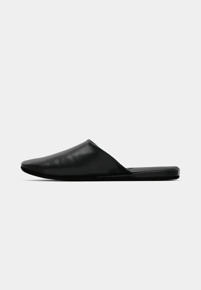 Mule noir en cuir à enfiler avec un bout pointu et une semelle plate, présenté en profil latéral sur un fond blanc uni.
