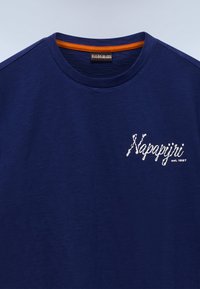 Μπλε ναυτικό T-shirt με λαιμόκοψη, με λευκό κείμενο "Napapijri est. 1987" στο αριστερό μέρος του στήθους και πορτοκαλί εσωτερικό περιθώριο στον γιακά.