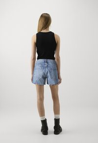 Svart ärmlös topp, högmidjade ljusblå denimshorts med fransad kant, i kombination med svarta ankboots och vita ankelsockar.