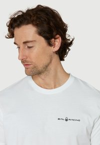 Vit bomull T-shirt med "SAIL RACING"-logotyp i svart, rund hals, kortärmad och en slät, jämn textur.