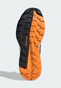 Semelle de chaussure présentant une surface texturée avec un grip en caoutchouc noir et orange. Dessins de bande de roulement distincts pour une meilleure traction, avec un détail de logo en relief.