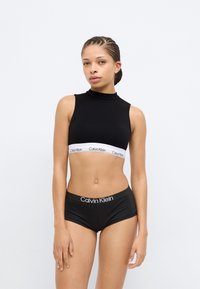 Μαύρο αμάνικο crop top με ψηλό λαιμό και λευκή ταινία Calvin Klein. Μαύρο σορτς με λογότυπο Calvin Klein στη μέση.