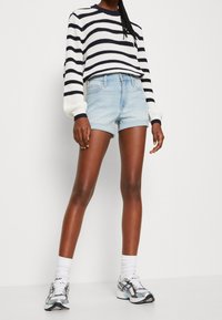 Suéter de punto a rayas en blanco y azul marino, combinado con pantalones cortos de mezclilla azul claro. Transición a zapatillas deportivas grises y azules con calcetas blancas.