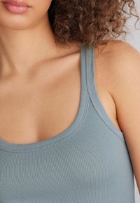 Světlomodrý žebrovaný top bez rukávů s kulatým výstřihem a tenkými ramínky, který představuje jemnou strukturu a těsný střih.