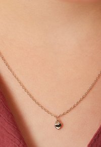 Zilveren ketting met een kleine, glanzende hartbedel. De ketting heeft ovale schakels en hangt net boven het sleutelbeen.
