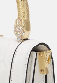 Valkoinen quiltattu käsilaukku mustalla reunalla, jossa on kultainen käärme-otanta, joka on koristeltu kirkkailla jalokivillä ja kultaisella lukolla. Suloinen nahkapinta.