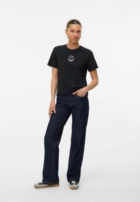 Zwarte katoenen t-shirt met een witte smiley-gezicht grafiek, gecombineerd met donkerblauwe wijde jeans en casual sneakers.