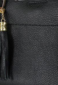 Zwarte handtas van getextureerd leer met gouden hardware en kwastaccent. Heeft een gestructureerde vorm en zichtbare stikseldetails.