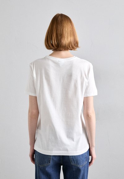 Camiseta blanca de manga corta con cuello redondo, de material de algodón ligero y un ajuste relajado, combinada con vaqueros de mezclilla azules.