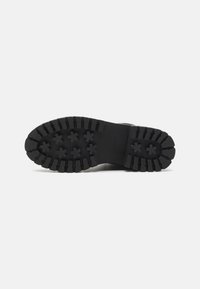 Suela de zapato de goma negra con un patrón de relieve profundo, que presenta acentos en forma de estrella y bordes estriados para mejorar el agarre y la tracción.