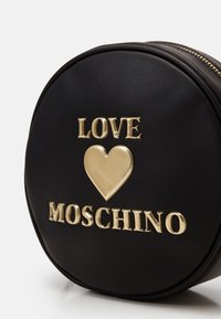Borsa rotonda nera in pelle sintetica con scritte dorate "LOVE" e "MOSCHINO" e un cuore dorato in evidenza, chiusura con zip e superficie testurizzata.