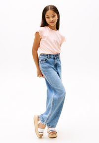 Lichtroze T-shirt met korte mouwen en gerimpelde randen, gecombineerd met een high-waisted, wijde pijpen blauwe spijkerbroek en witte sandalen met plateauzool.