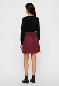 Jupe en suédine bordeaux avec un design à volants, une taille élastique et une longueur au-dessus du genou, associée à un haut noir à manches longues et des bottes noires.