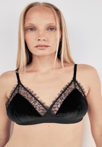 Reggiseno nero con design a triangolo, arricchito da dettagli in pizzo e texture morbida in velluto. Spalline regolabili e rifinitura in pizzo intricata.