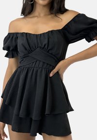 Zwarte off-shoulder peplum top met korte pofmouwen, gestructureerde stof en een getailleerde taille, voorzien van gelaagde ruches aan de zoom.