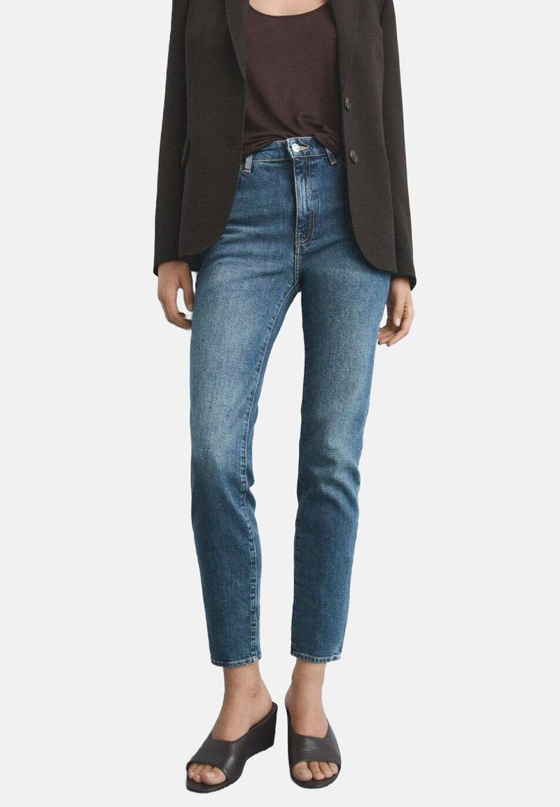 Höga blå denimjeans med slim fit, med fem fickor och knappstängning, i kombination med en svart kavaj och öppna klacksandaler.
