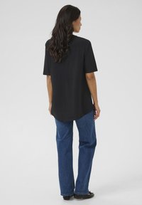 Camisa negra de manga corta con dobladillo curvo, combinada con jeans azules de pierna recta. La tela parece suave, con un ajuste relajado y mínimos detalles.