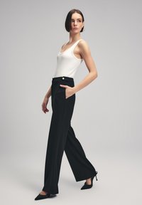 Pantaloni neri a gamba larga con tasche frontali e dettagli con bottoni dorati, abbinati a una canotta bianca a coste. Tessuto liscio con un design strutturato.