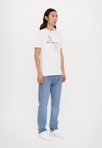 Fehér pamut póló, szürke "Armani Exchange" logóval és grafikai mintával. Világoskék farmerkabát és fehér sportcipő kíséri.
