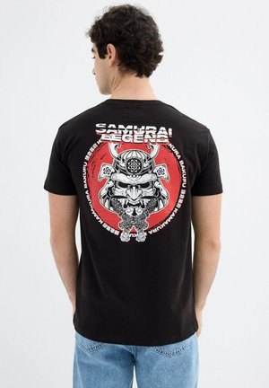 Camiseta negra con una gran ilustración de una máscara de samurái en la parte trasera, rodeada por un círculo rojo y texto, hecha de tela de algodón.