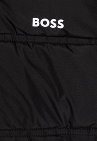 Černá tkanina s elastickým šitím a výrazným bílým textem "BOSS" vytištěným blízko horního středu.