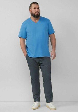 Blaues V-Ausschnitt-T-Shirt, kurze Ärmel, kombiniert mit grauen Hosen. Der Stoff scheint glatt zu sein, mit einer lockeren Passform und minimaler Detailgebung. Weiße Sneaker.