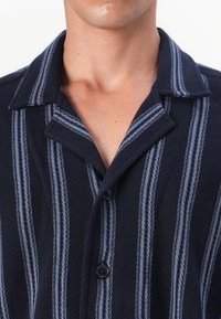 Camisa de botones azul marino con rayas verticales en azul claro y blanco, textura suave y cuello puntiagudo. Botones negros en la parte delantera.