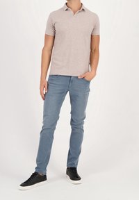 Svetle šedé texturované polo tričko, slim-fit modré džíny a černé tenisky s bílou podrážkou. Model stojí s jednou rukou v kapse.